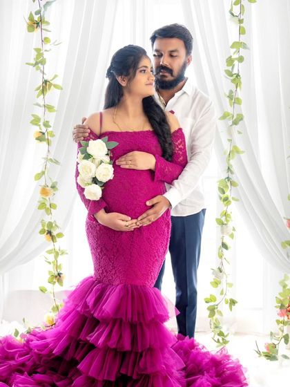 A romantic portrait of a couple surrounded by floral vines, the mom-to-be holding a bouquet of white roses.