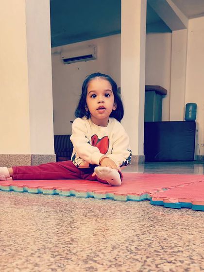 A young student practices a split on the mat. We introduce basic gymnastic stretches to improve flexibility from an early age.
