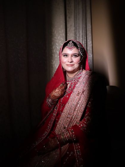 A smiling portrait of the bride. The soft lighting enhances her radiant makeup and the intricate details of her red bridal attire.