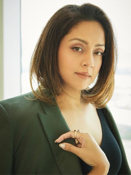 A close-up portrait that captures Jyotika's confident and direct gaze, with the blazer draped over her shoulder.