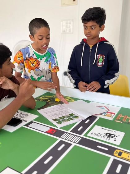 A team of three students engaged in a lively discussion over the IRO rulebook and challenge mat. Understanding the rules and scoring is just as important as building a great robot.