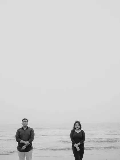 A minimalist black and white photograph using negative space to create a sense of calm and isolation. The couple stands by the sea, creating a simple yet powerful and artistic portrait.