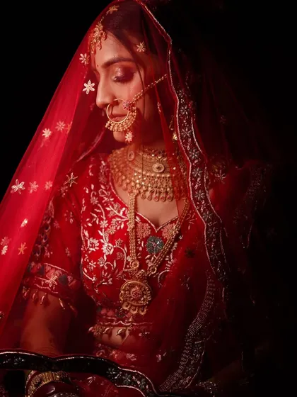 We love playing with light and shadow to create stunning bridal portraits. This shot uses a single light source to sculpt the bride's features and highlight the rich details of her red wedding lehenga, creating a timeless and artistic image.