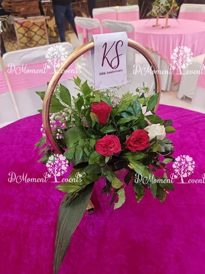 A custom table centerpiece for the 50th anniversary. A beautiful arrangement of red and white roses is set within a golden ring holder that features the couple's initials and anniversary date.