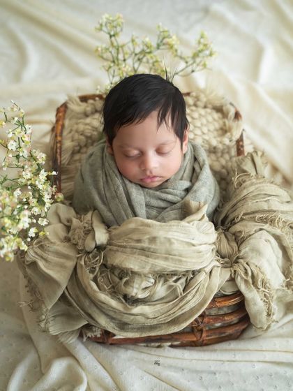 This baby boy is nestled in a rustic basket with soft, neutral green and beige wraps. The delicate white flowers add a touch of lightness.