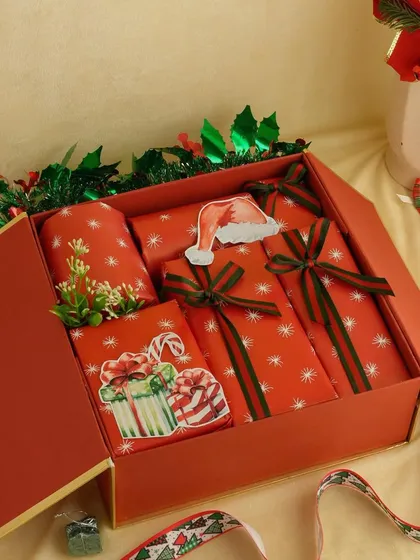 A beautifully wrapped Christmas gift box in festive red paper. The 'exploding box' design reveals multiple layers of gifts inside.