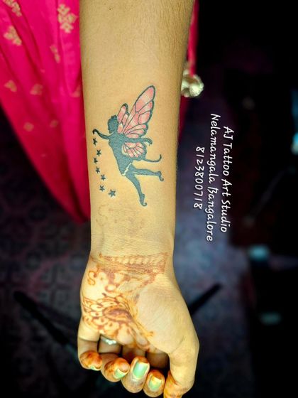 A whimsical fairy tattoo with pink wings on the wrist.