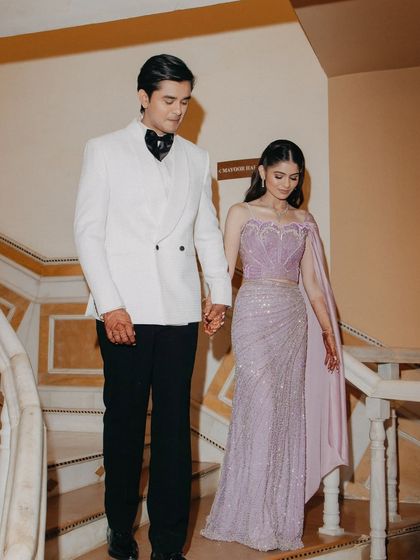 An elegant shot of the couple descending a staircase hand-in-hand, showcasing their coordinated and stylish Sangeet outfits.