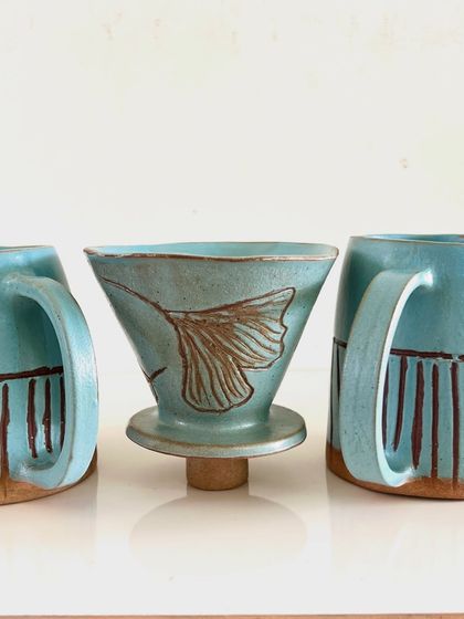 This pour-over coffee dripper and matching mugs were created by a student. The pieces are decorated with carved lines and a beautiful turquoise glaze.