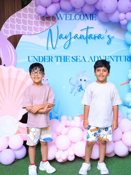 Two friends pose in front of the mermaid backdrop. Our parties are a great place for kids to celebrate together.