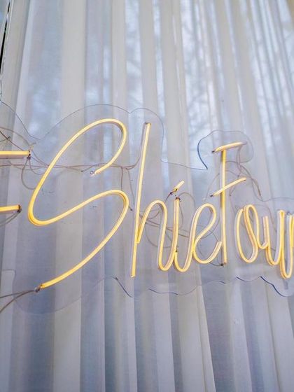 A custom neon sign with the couple's wedding hashtag, #SheFoundAMan. This modern detail adds a fun and personal touch to the elegant white curtain backdrop.