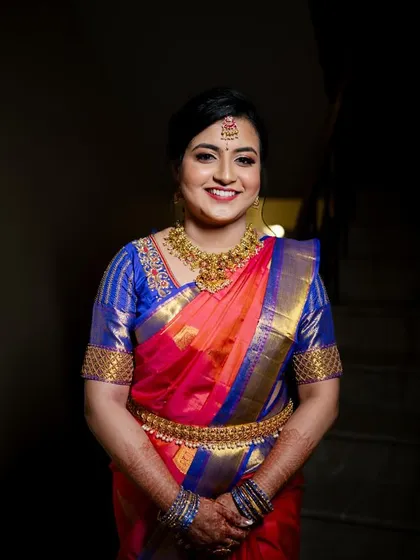 A radiant smile for an engagement ceremony. This classic South Indian look features a flawless base, defined eyes, and a joyful red lip, perfectly complementing the vibrant silk saree and traditional temple jewellery.