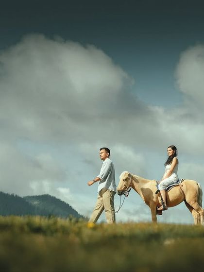 A cinematic shot of the couple on their journey, him leading her trusted steed across a vast, green landscape. This image tells a story of adventure and companionship, perfect for a fairytale pre-wedding theme.