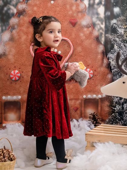 A cozy winter scene, with this little girl in her red velvet dress exploring a gingerbread house wonderland.