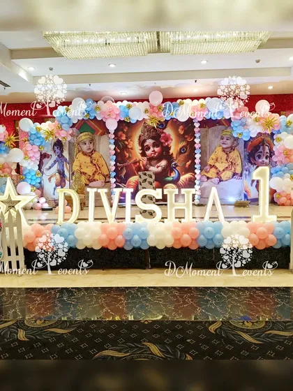 A full view of the Krishna-themed stage, featuring a large backdrop with images of the birthday girl dressed as Krishna, marquee letters, and extensive balloon decorations.