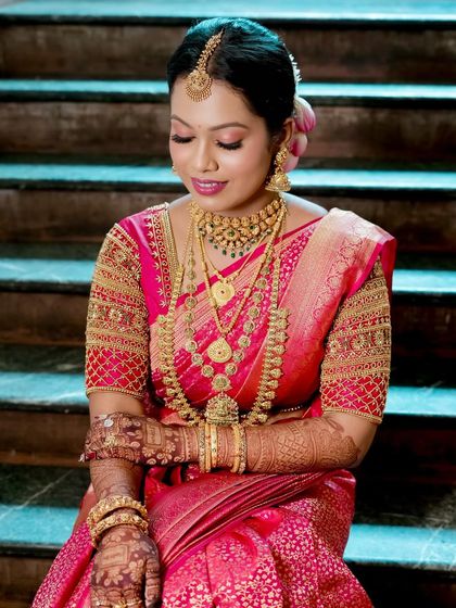 Seated on the steps, Lavanya's entire look comes together. The glowing base, traditional gold jewelry, and lotus-adorned hair create pure bridal magic.