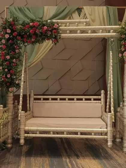 For a touch of timeless elegance, we created this seating area for a mom-to-be. The design features a classic white swing decorated with lush pink and red floral arrangements and soft, sage green draping, providing a beautiful and comfortable spot for photos and relaxation.