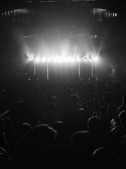 A powerful black and white shot of the stage lights cutting through the darkness, illuminating the massive crowd.