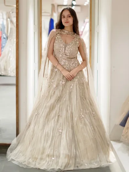 A full, poised shot of the beige gown with its elegant cape. The high neckline and flowing tulle create a look that is both regal and modern, ideal for an engagement ceremony.