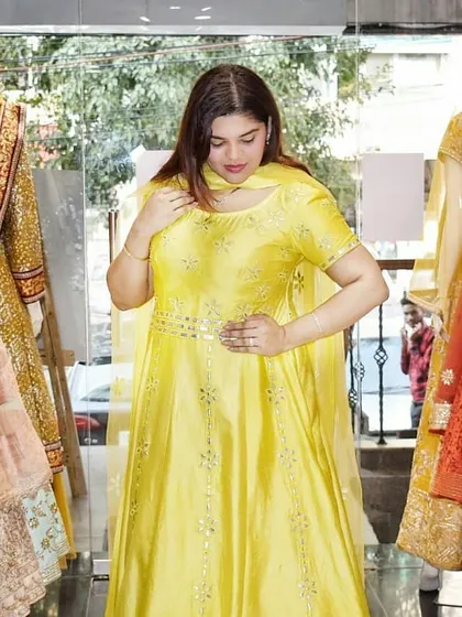 A customer trying on a bright yellow Anarkali with delicate mirror work. This cheerful and sunny outfit is perfect for a Haldi or Mehendi ceremony.