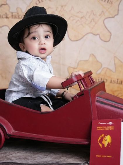 A curious little traveler looks on during his adventure-themed photoshoot, sitting in a vintage-style toy car.