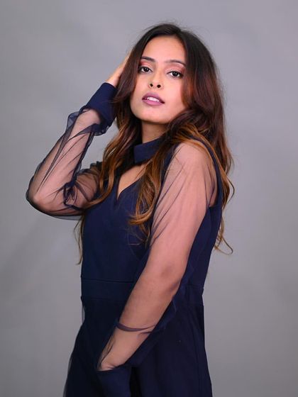 A model posing in a navy blue dress with sheer sleeves. The pose is elegant and ideal for a sophisticated fashion portfolio.