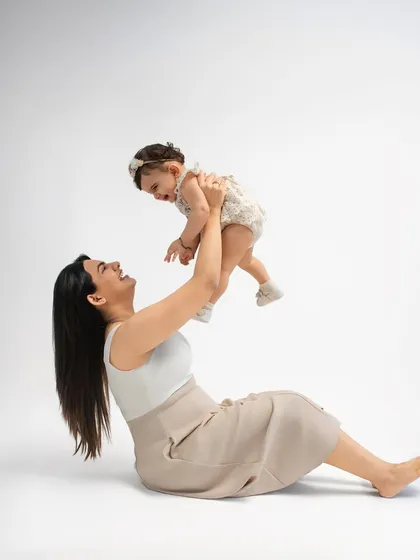 A mother sits on the floor, lifting her laughing baby into the air. These simple, joyful moments are the ones you'll cherish most.