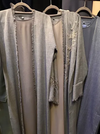 These grey abayas showcase different textures and details. One has frayed edges for a modern look, while another features subtle floral embroidery on the sleeves.