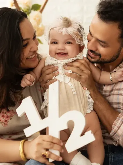 Celebrating a half-birthday with the number "1/2" prop. This family portrait captures the baby girl's happy milestone with her loving parents.