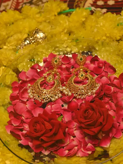 The 'मणिकर्णिका' (Manikarnika) earrings displayed on a bed of rose petals, highlighting their beauty and craftsmanship.
