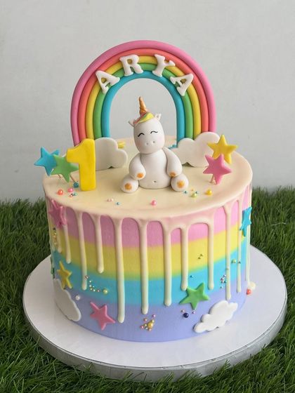 This rainbow drip cake is a perfect match for a unicorn theme. The cake features rainbow-colored whipped cream stripes, a white chocolate drip, and is topped with a handmade fondant unicorn and rainbow.