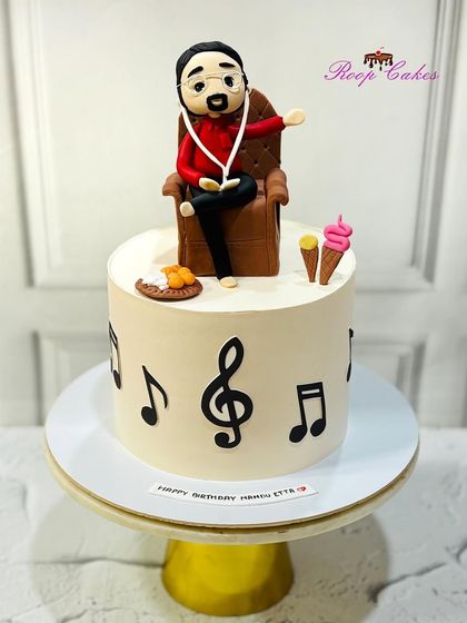 A cake for a music lover. This design features musical notes around the side and is topped with a custom fondant figure relaxing in a chair, listening to music, and enjoying his favorite snacks.