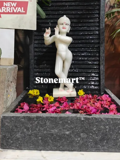 The white marble Kanha Ji statue stands out beautifully against the dark granite waterfall. This 3-foot fountain is suitable for wall-mounted placement in a living room, balcony, or garden.