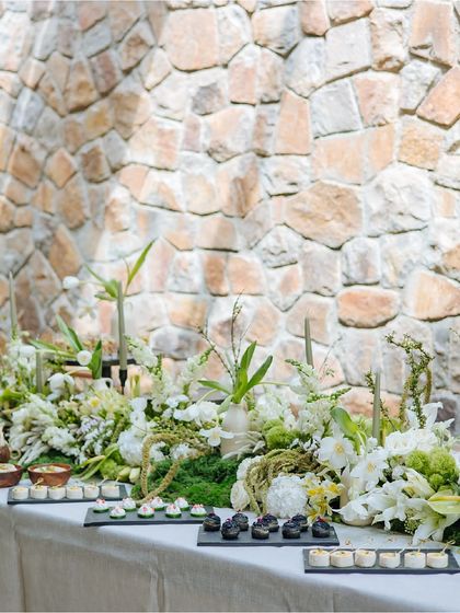 An overview of our Earth Table setup, showing delicate canapés arranged on slate platters. The table is adorned with a lush centerpiece of moss, white lilies, and other greenery.