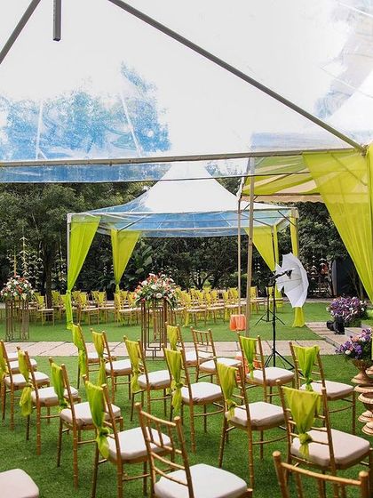 A wide view of a naming ceremony setup under a clear-top tent. The bright green and yellow decor adds a pop of color against the natural greenery.