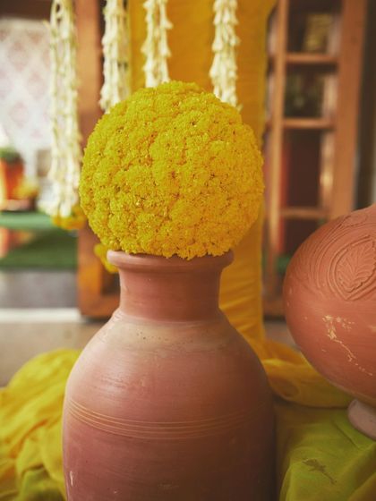 A close-up of a 'genda phool' sphere placed on a terracotta pot. This simple yet beautiful detail is a staple of my traditional Haldi decor designs.