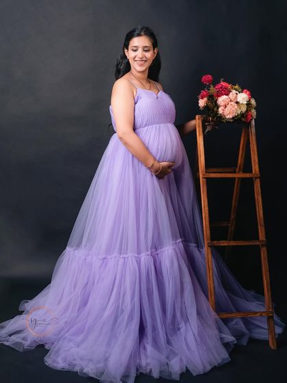 A serene solo portrait of a mom-to-be in a lavender gown, standing next to a rustic ladder prop adorned with flowers.