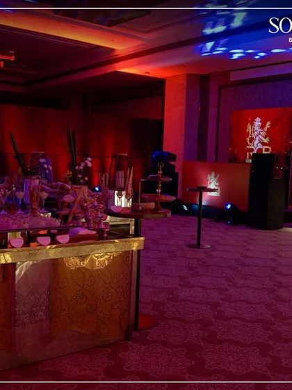 An overview of the lounge and buffet area for a celebratory soirée, with ambient red and blue lighting creating a vibrant mood. We manage every aspect of the event's food and beverage experience.