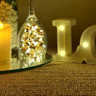 A close-up of our creative lighting solutions. Here, we've filled a wine glass with sparkling confetti and fairy lights, placed next to an LED candle and marquee letter for a dazzling effect.