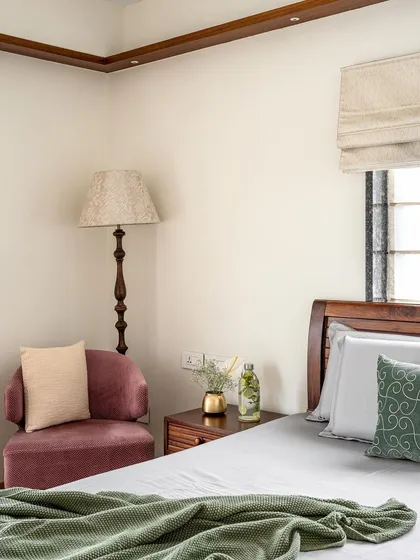 The parent's room in 'Gulmohar' features a neutral palette, a custom bed, and a cozy reading corner with an armchair and floor lamp.