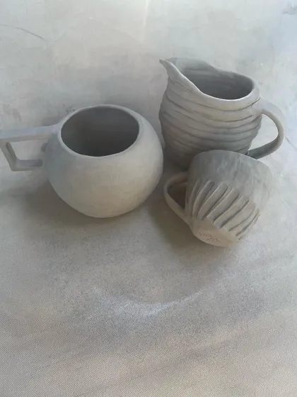 Another angle of the unfired hand-built mugs and pitcher. This view highlights the different handle styles and surface textures created by students in the beginner course.