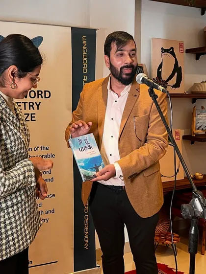 A winner shares his own published book with the audience, a testament to his continued journey in poetry.