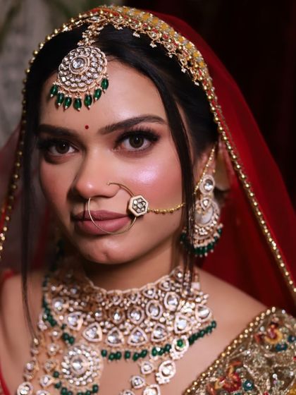 A classic bridal portrait. The traditional red dupatta frames the face, while the green jewelry provides a beautiful contrast.