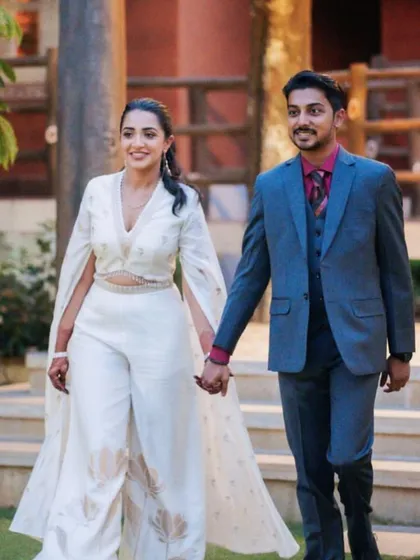The couple making a stylish entrance to their Sangeet. The bride's chic white jumpsuit with a cape is a perfect example of modern wedding fashion.