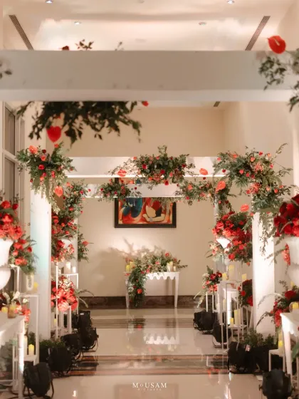 An elegant floral archway welcomes guests to the wedding. The beautiful arrangement of red and green florals against a white structure creates a stunning entrance and a perfect photo opportunity.