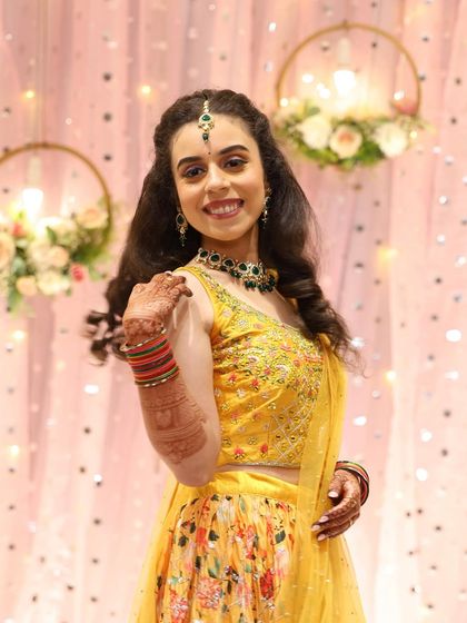 The bride looking radiant in her yellow floral lehenga for the sangeet. The makeup is fresh and bright, with a pop of color from the green jewelry.