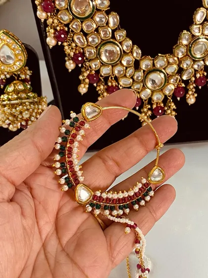 A close-up of a traditional bridal nath with red, green, and white beads. This is a key piece of bridal jewellery and is available for rent.