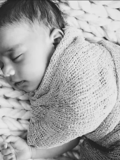 A peaceful newborn sleeps soundly, swaddled in a soft, chunky knit blanket. This black and white photo emphasizes the serene and delicate nature of your baby's first days.