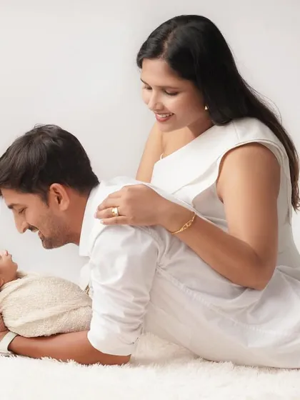 A relaxed and loving pose with mom and dad admiring their newborn baby. The simple white outfits and soft rug create a clean, timeless family portrait.