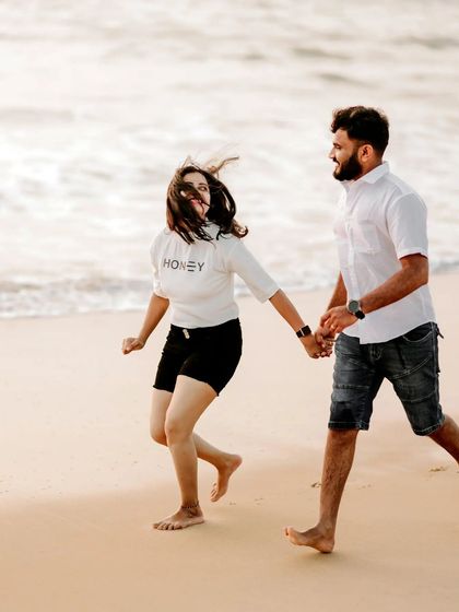 A playful moment on the beach, with a couple running hand-in-hand, their joy evident.